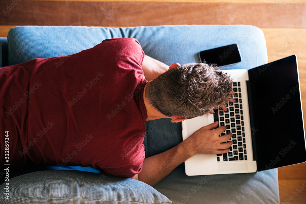 Casual male remote worker on sofa with laptop - obrazy, fototapety, plakaty 