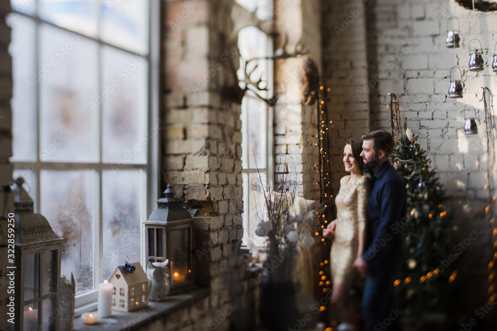 Obraz premium Celebrating Christmas together. Young caucasian couple in holiday clothes hugging near the Christmas tree. New Year, Valentine, love, romance concept.