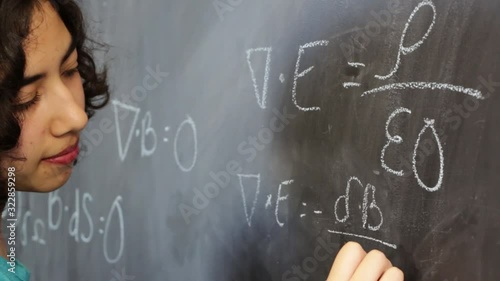 Smart young latin woman writing Maxwell's equations on chalkboard photo