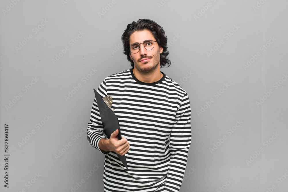 Young employee man holding an inventory unhappy looking in camera with sarcastic expression. Young employee man holding an inventory unhappy looking in camera with sarcastic expression.