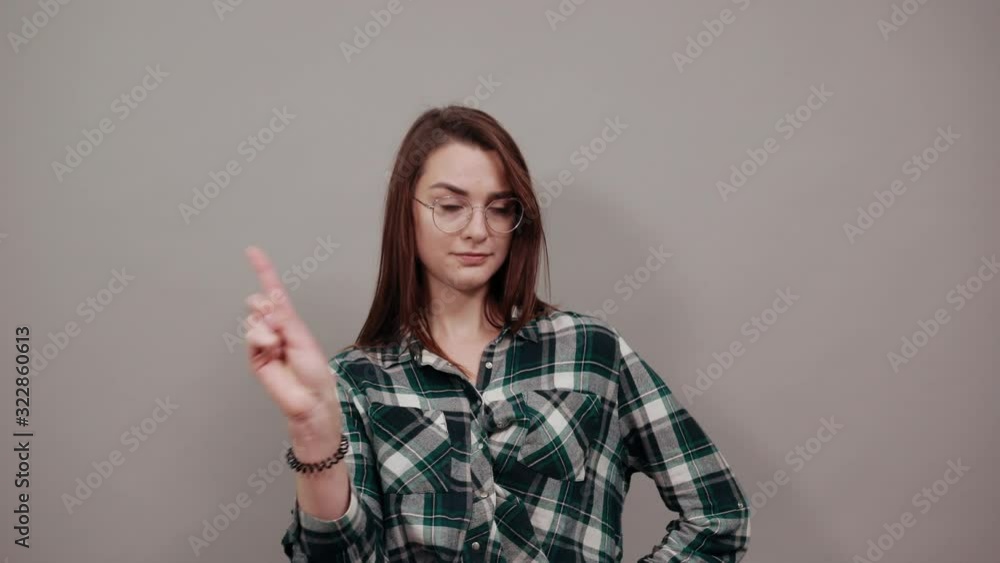 Young brunette girl blue green in checked shirt on grey background woman in glasses counteracts by shaking her index finger, a sign of disagreement Young brunette girl blue green in checked shirt on grey background woman in glasses counteracts by shaking her index finger, a sign of disagreement