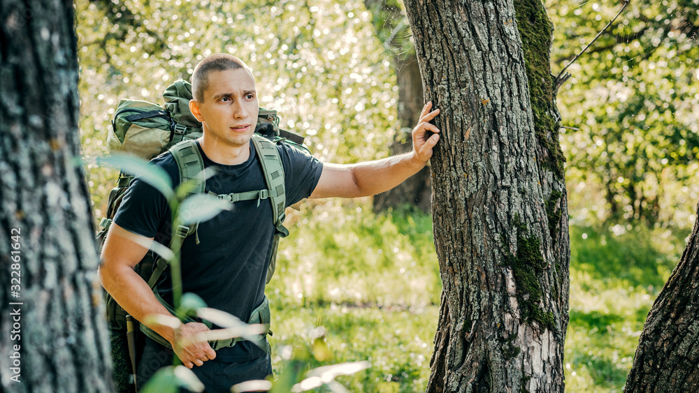 Portrait of a male tourist with a backpack standing in the woods. Standing against the forest Portrait of a male tourist with a backpack standing in the woods. Standing against the forest