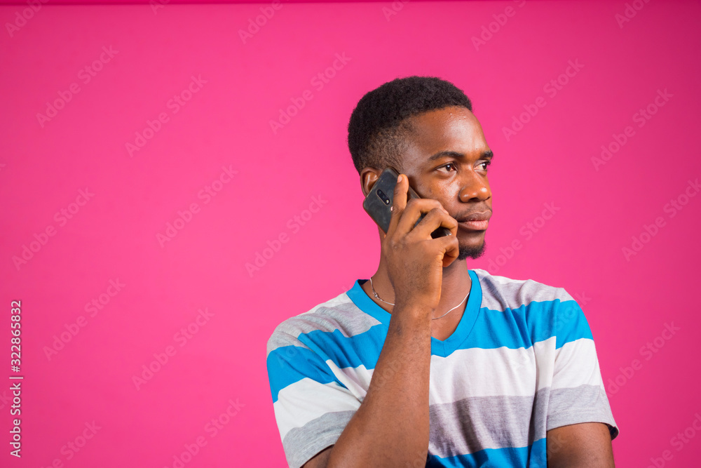 a young nigerian man wearing strips cloth isolated over pink background feeling confident about the call he his receiving on his smart phone a young nigerian man wearing strips cloth isolated over pink background feeling confident about the call he his receiving on his smart phone