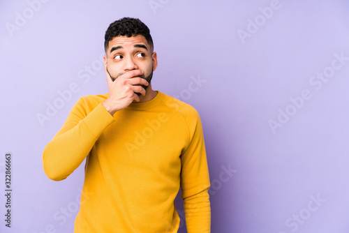 Young mixed race arabic man isolated thoughtful looking to a copy space covering mouth with hand.