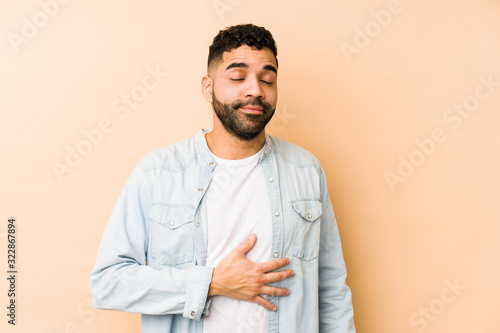 Young mixed race arabic man isolated touches tummy, smiles gently, eating and satisfaction concept.