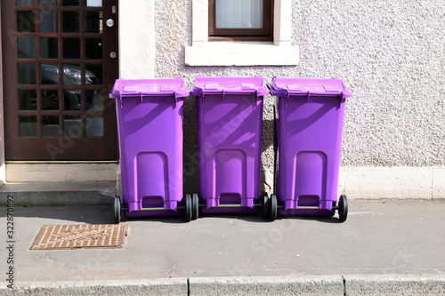 Three Purple Plastic Wheelie Bins on Sunny Pavement 