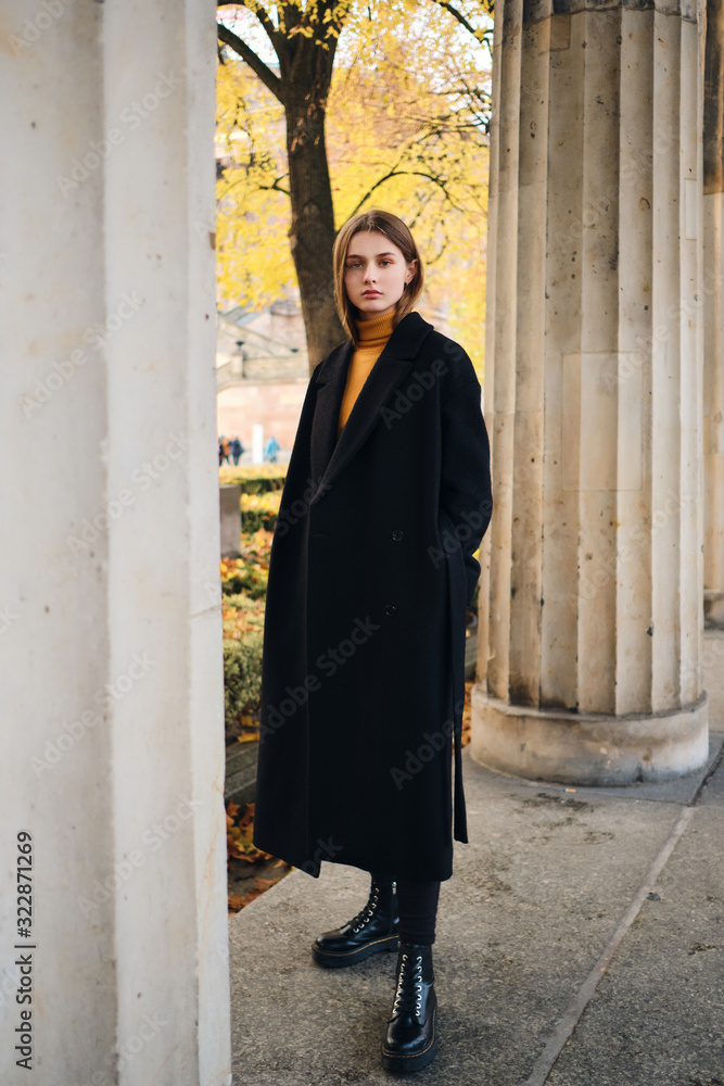 Attractive girl in black coat intently looking in camera outdoor