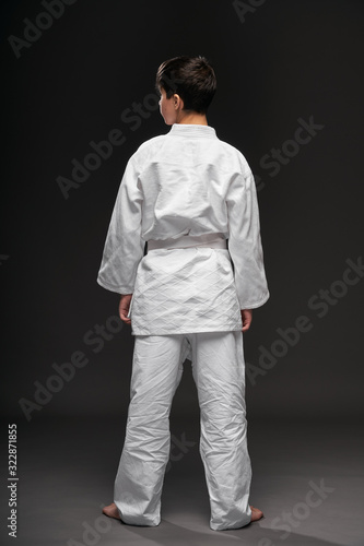 backside view of a teenager dressed in martial arts clothing poses on a dark gray background, a sports concept