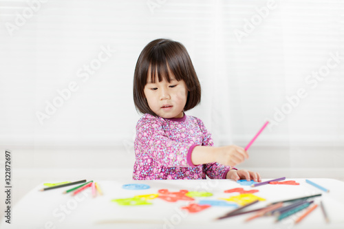 toddler girl practice writing letters on white paper against white background