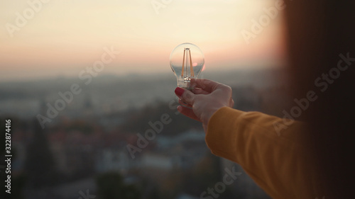 Close up hands woman holds a house light bulb at sunset renewable energy nature electricity innovation green invention responsibility environment adult power protect lamp slow motion