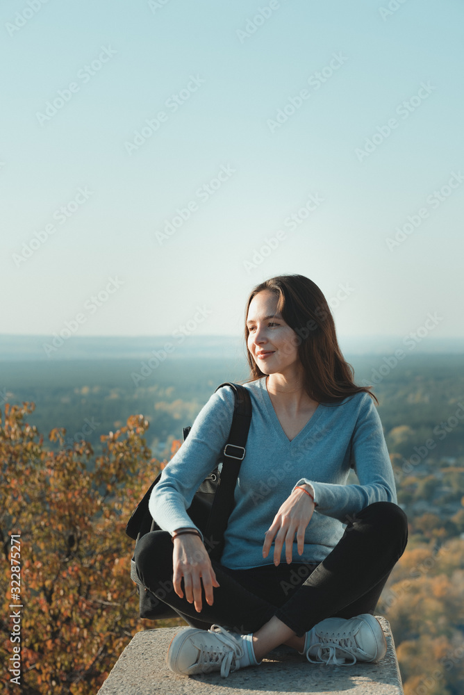 Pretty girl sits on a high hill and smiles. Viewpoint. Vertical frame