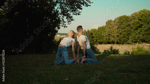 Caucasian fitness couple training yoga poses together bending back exercises on mat in the park at sunrise. Sport strecthing concept.