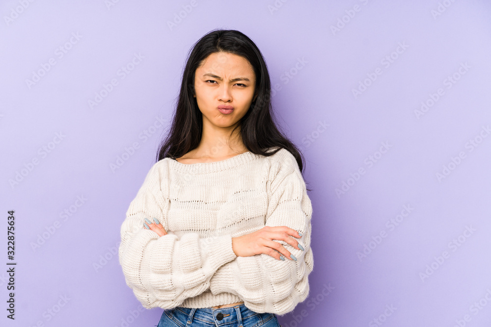 Young chinese woman isolated on a purple background frowning face in displeasure, keeps arms folded. Young chinese woman isolated on a purple background frowning face in displeasure, keeps arms folded.