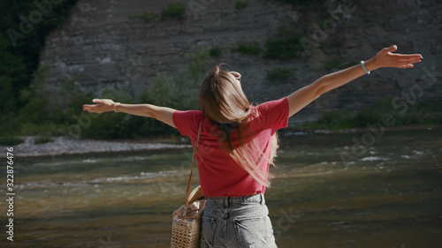Shot back attractive young woman with her hands raised stand near river forest outdoor travel adventure female tourist water beautiful tourist relaxation freedom landscape slow motion