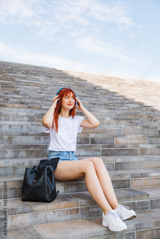 Fototapeta premium Young woman sits on stairs listening to music