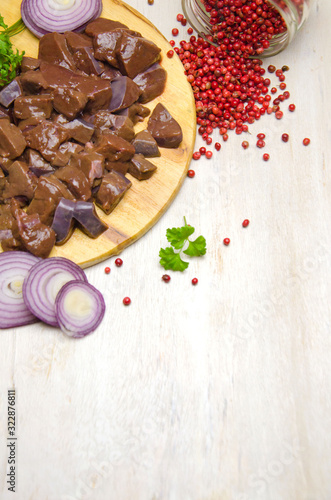 fresh chunks of beef liver on a cutting Board next to onions and spices on a wooden white table selective