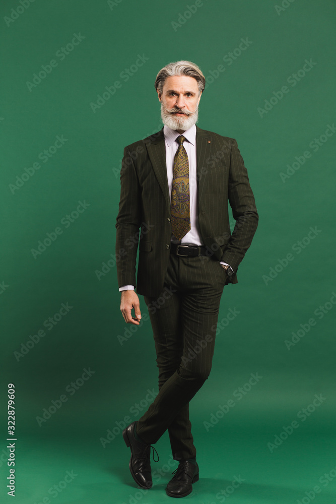 Stylish bearded middle-aged man in khaki suit on green background Stylish bearded middle-aged man in khaki suit on green background