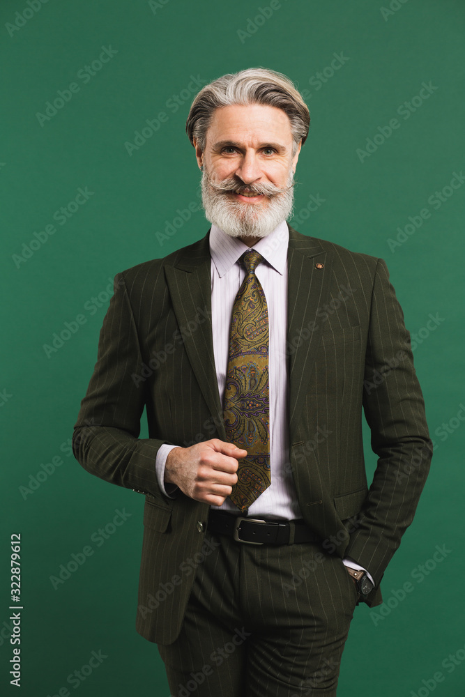 Stylish bearded middle-aged man in khaki suit on green background Stylish bearded middle-aged man in khaki suit on green background