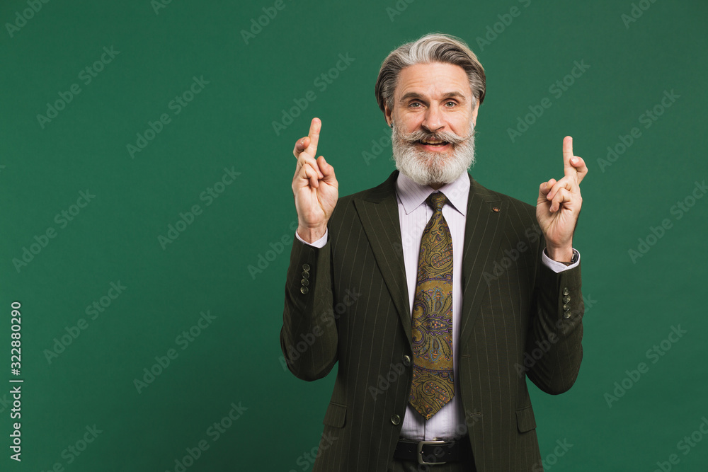 Bearded middle-aged man in suit crosses fingers for good luck on green background. Bearded middle-aged man in suit crosses fingers for good luck on green background.