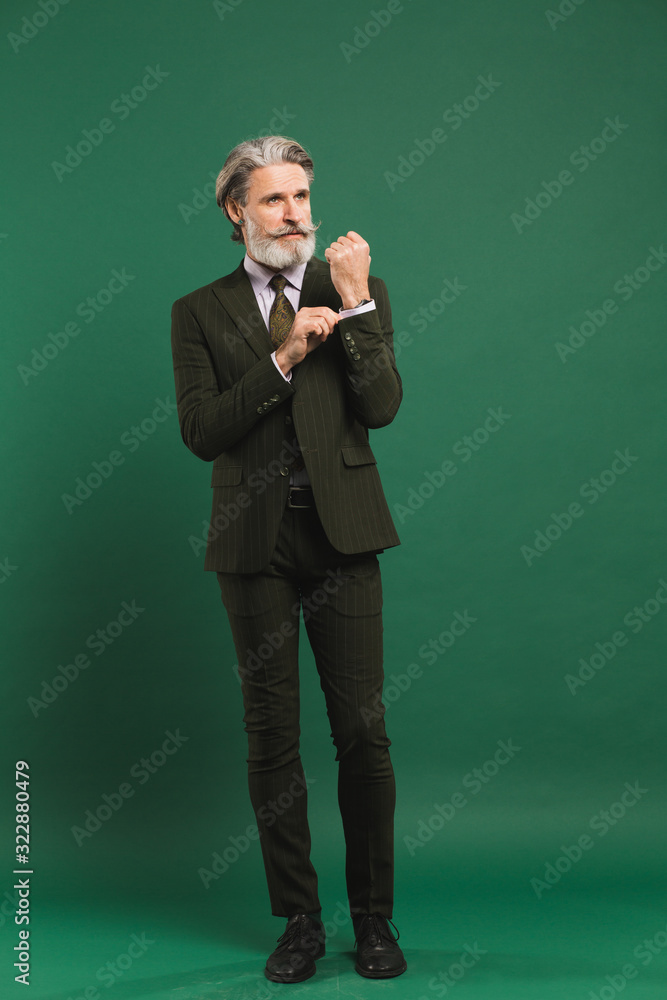 Stylish bearded middle-aged man in khaki suit on green background Stylish bearded middle-aged man in khaki suit on green background