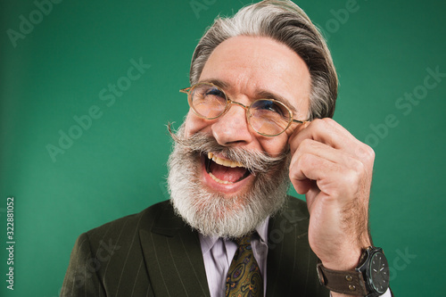 Funny stylisg man who holds and shows mustache and beard on green background photo