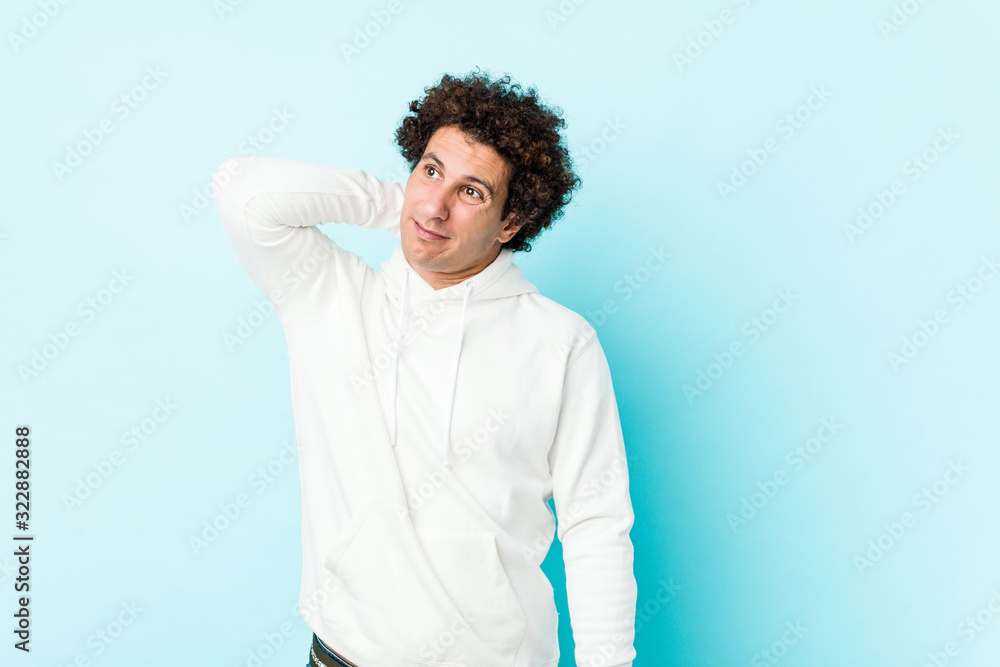 Young sporty man against a blue background touching back of head, thinking and making a choice. Young sporty man against a blue background touching back of head, thinking and making a choice.
