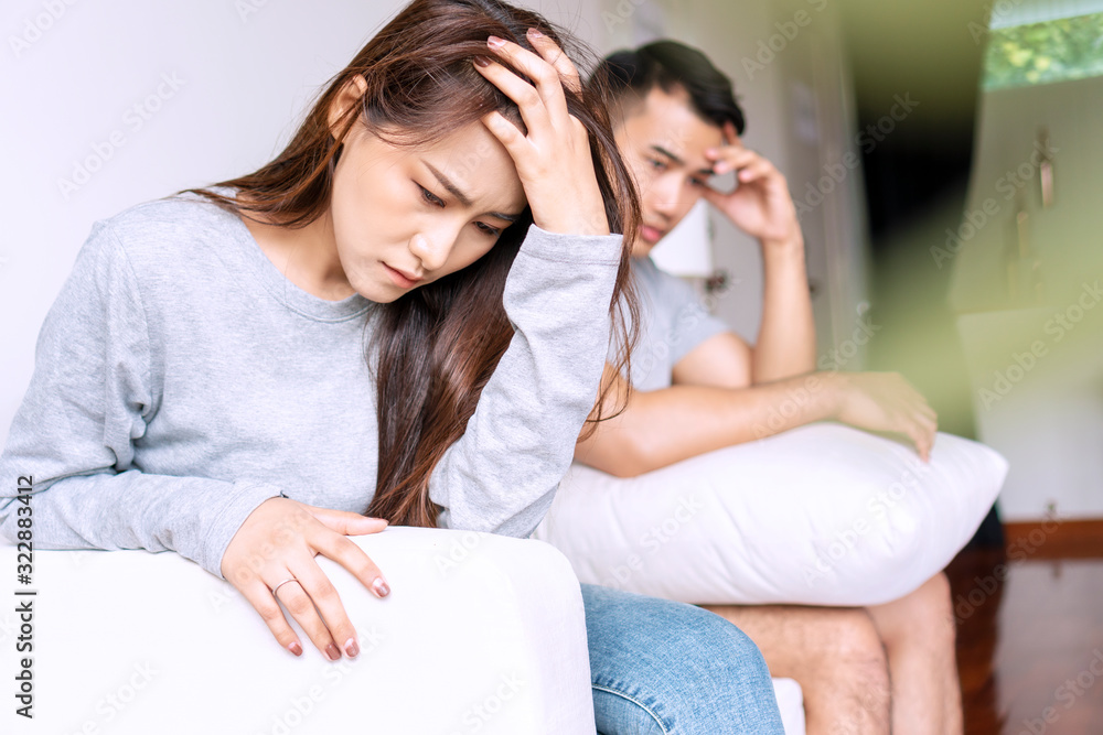 Unhappy young woman sitting on sofa with boyfriend while stress not talking after fight in living room. Upset wife thinking with her husband sitting on sofa. Relationship problem lover concept. Unhappy young woman sitting on sofa with boyfriend while stress not talking after fight in living room. Upset wife thinking with her husband sitting on sofa. Relationship problem lover concept.