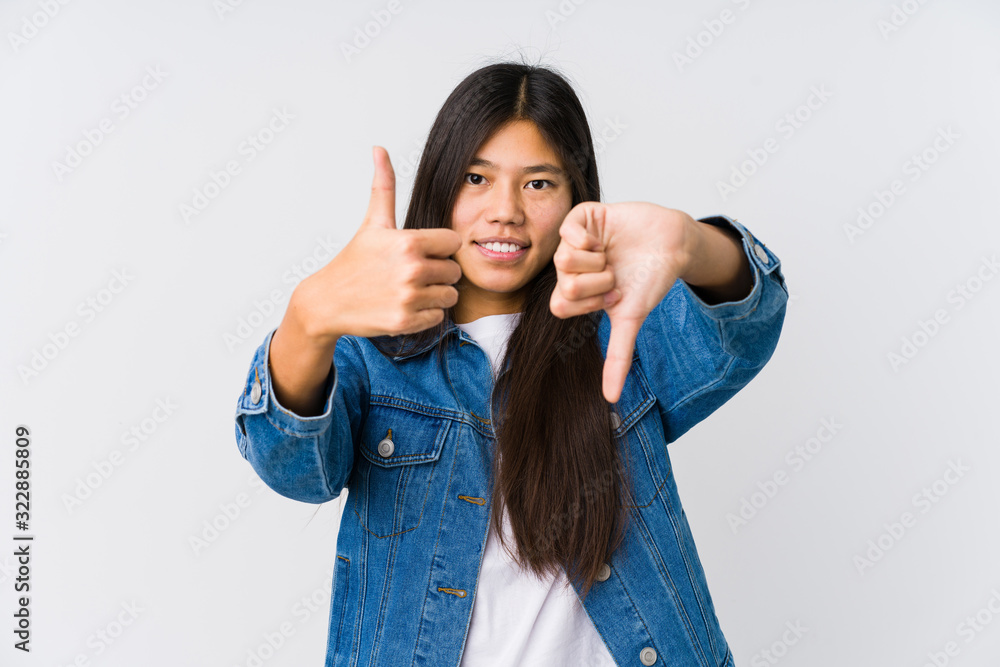 Young asian woman showing thumbs up and thumbs down, difficult choose concept Young asian woman showing thumbs up and thumbs down, difficult choose concept