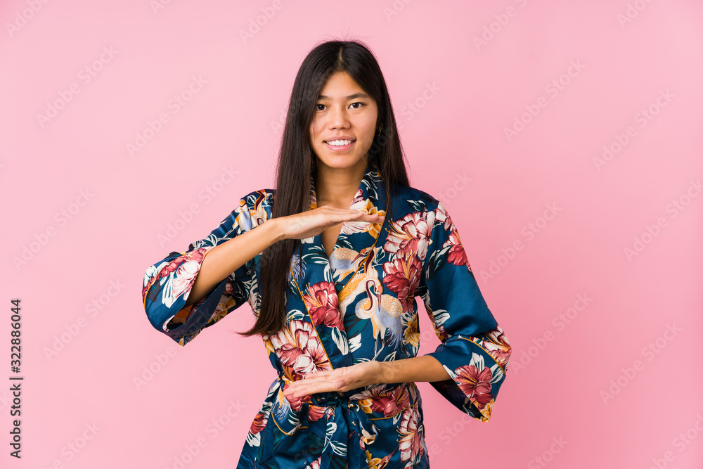 Young asian woman wearing a kimono pajamas holding something with both hands, product presentation. Young asian woman wearing a kimono pajamas holding something with both hands, product presentation.