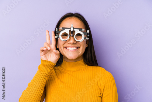Youn indian woman with optometry glasses showing victory sign and smiling broadly.
