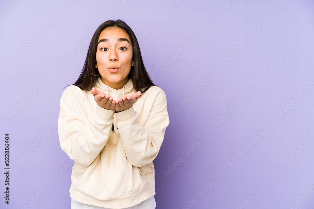 Young woman isolated on a purple background folding lips and holding palms to send air kiss. Young woman isolated on a purple background folding lips and holding palms to send air kiss.