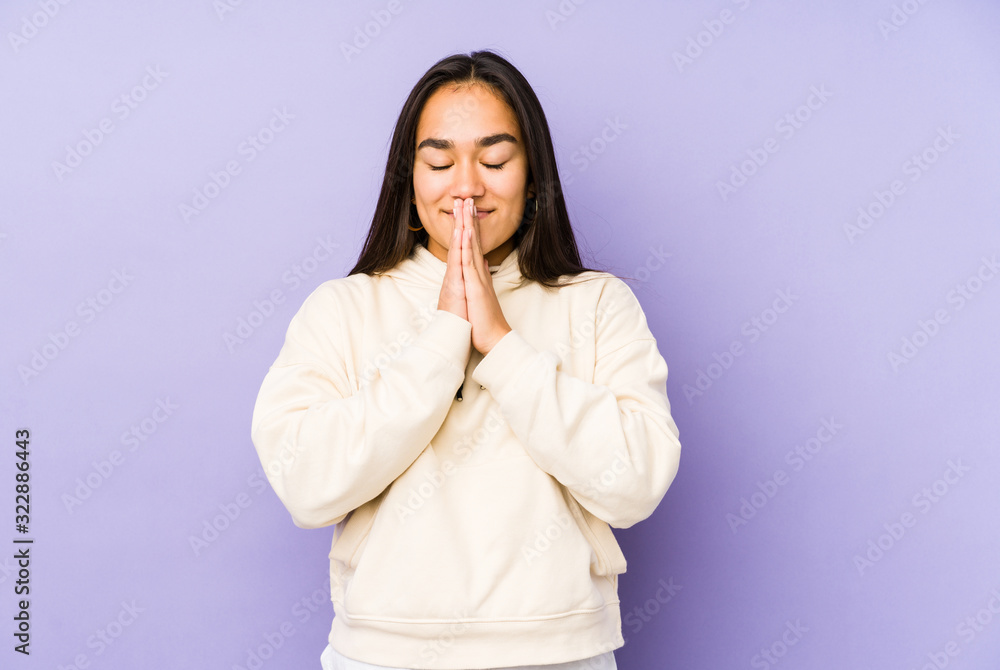 Young woman isolated on a purple background holding hands in pray near mouth, feels confident. Young woman isolated on a purple background holding hands in pray near mouth, feels confident.
