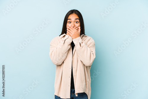 Young woman isolated on a blue background shocked covering mouth with hands.