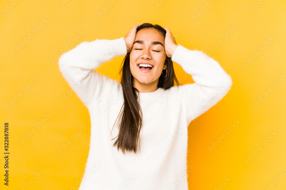Young woman isolated on a yellow background laughs joyfully keeping hands on head. Happiness concept. Young woman isolated on a yellow background laughs joyfully keeping hands on head. Happiness concept.