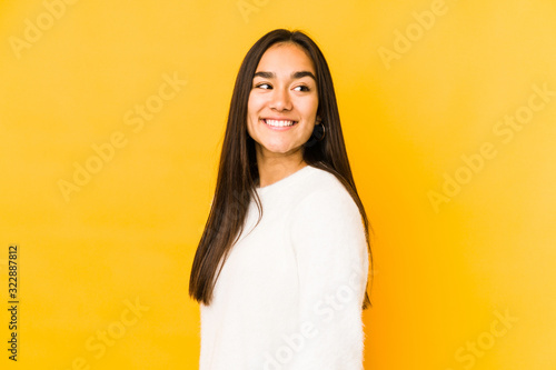 Young woman isolated on a yellow background looks aside smiling, cheerful and pleasant. © Asier