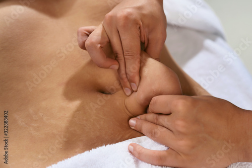 Masseur pulls hand the skin on the abdomen, showing the body fat in the abdominal area and sides. Treatment and disposal of excess weight, the deposition of subcutaneous fat.