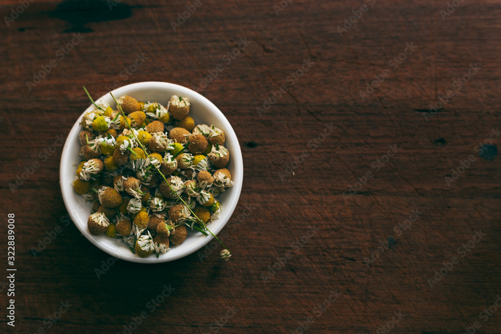 Bowl of dried chamomile flowers on a rustic timber chopping block in authentic flat lay with space for text Bowl of dried chamomile flowers on a rustic timber chopping block in authentic flat lay with space for text
