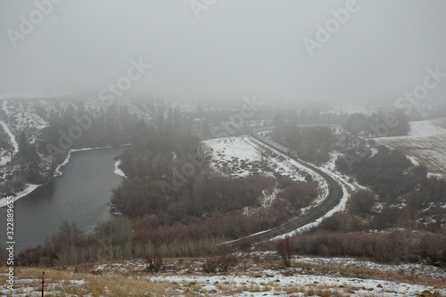 Train coming through the fog around a curve in a snow covered valley surrounded by trees and following a river