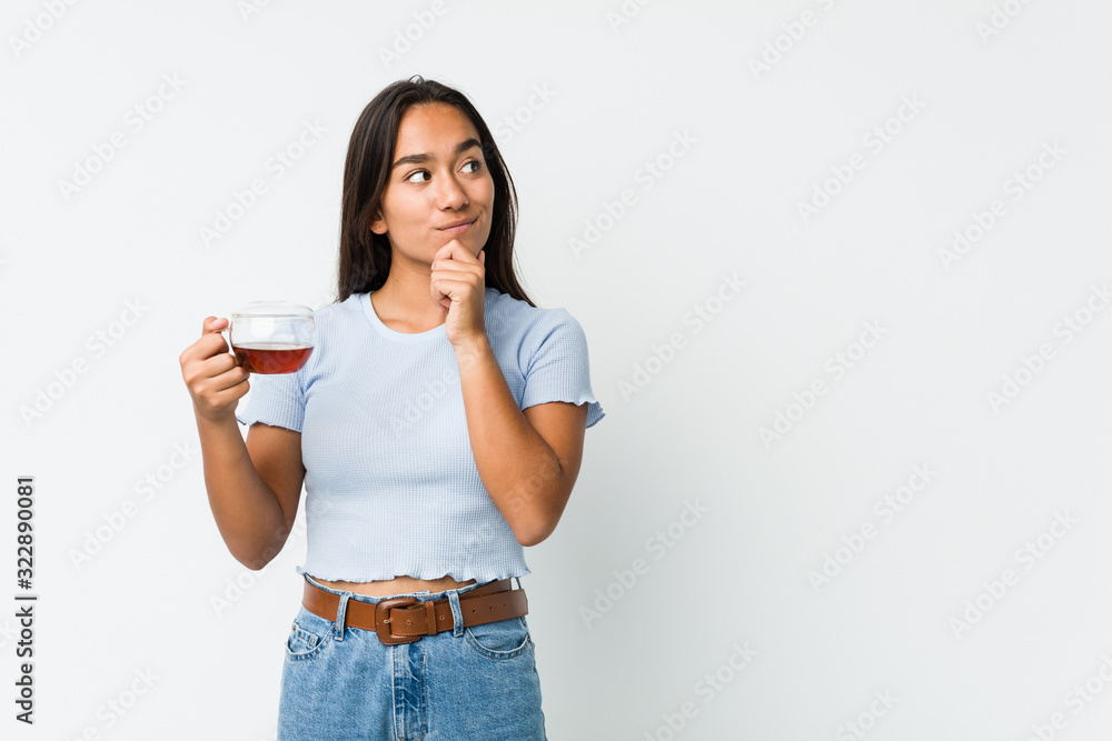 Young mixed race indian holding a tea cup looking sideways with doubtful and skeptical expression. Young mixed race indian holding a tea cup looking sideways with doubtful and skeptical expression.