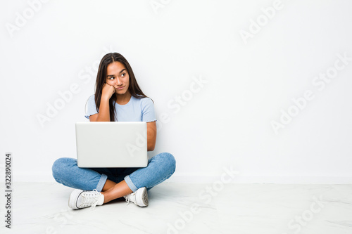 Young mixed race indian woman sitting working on laptop who feels sad and pensive, looking at copy space.