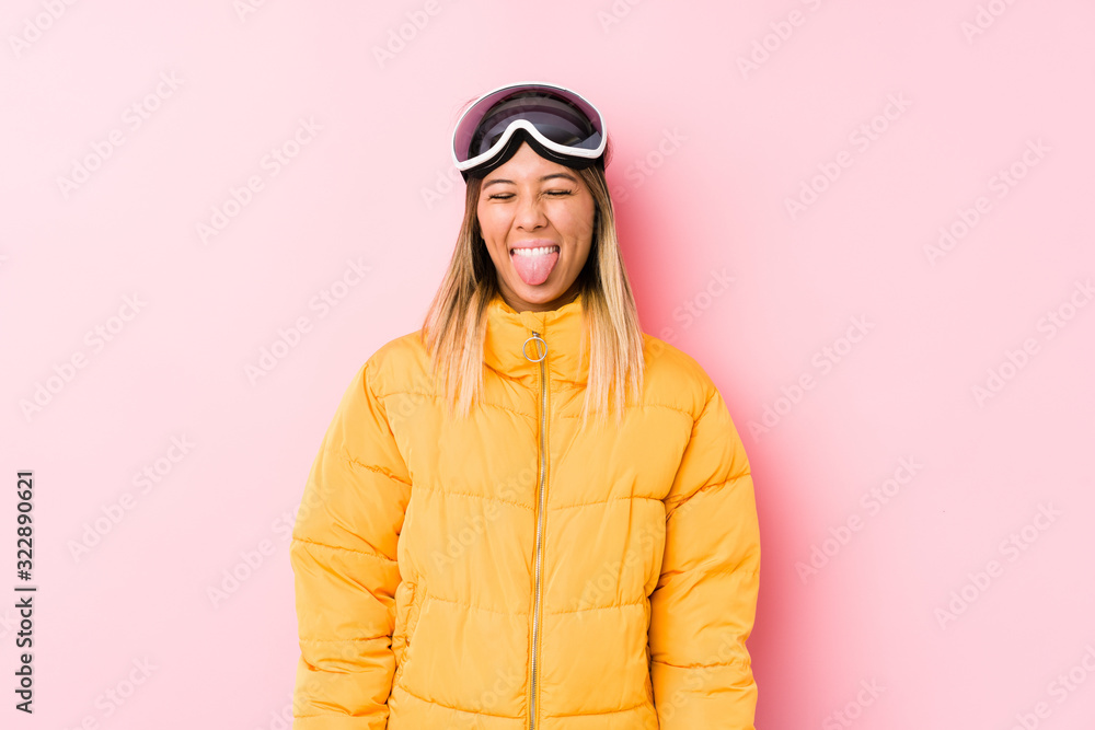 Young caucasian woman wearing a ski clothes in a pink background funny and friendly sticking out tongue.