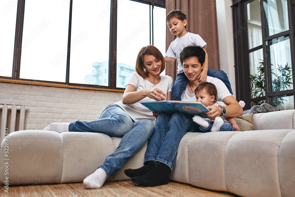 Happy international family concept. Dad, mom, son and little daughter posing for a camera at home, are engaged in home parenting. Home holidays, parenting, concept children and parents. Happy international family concept. Dad, mom, son and little daughter posing for a camera at home, are engaged in home parenting. Home holidays, parenting, concept children and parents.