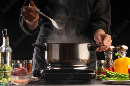 Culinary specialist or chef cooks soup or Italian pasta, from dressing. Heating a pan with steam, against a background of vegetables. Recipe book, cooking, gastronomy, freezing in motion.
