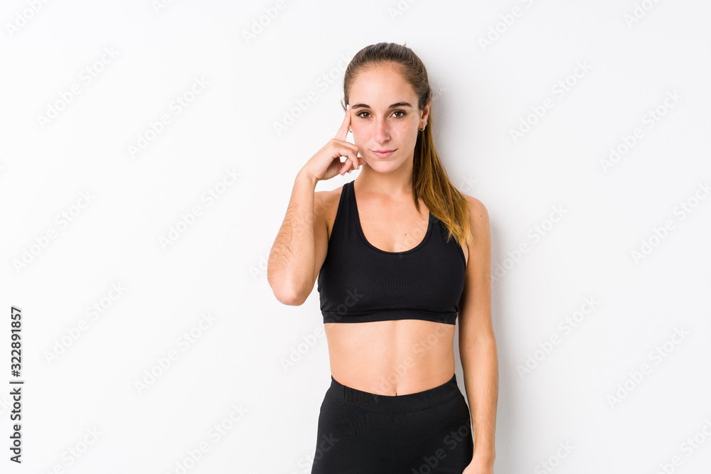 Young caucasian fitness woman posing in a white background pointing temple with finger, thinking, focused on a task. Young caucasian fitness woman posing in a white background pointing temple with finger, thinking, focused on a task.