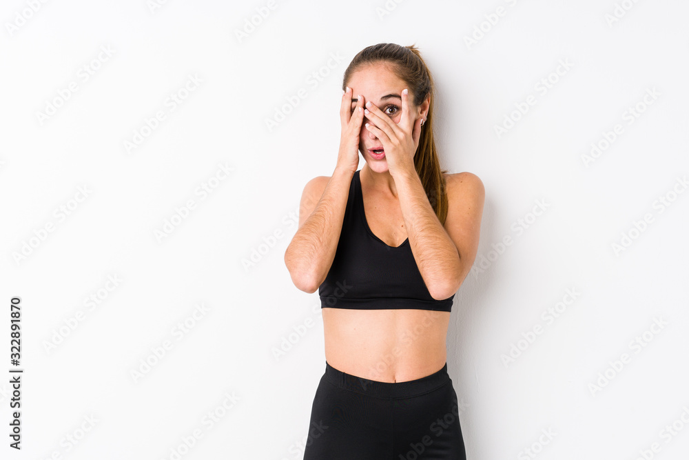 Young caucasian fitness woman posing in a white background blink through fingers frightened and nervous. Young caucasian fitness woman posing in a white background blink through fingers frightened and nervous.
