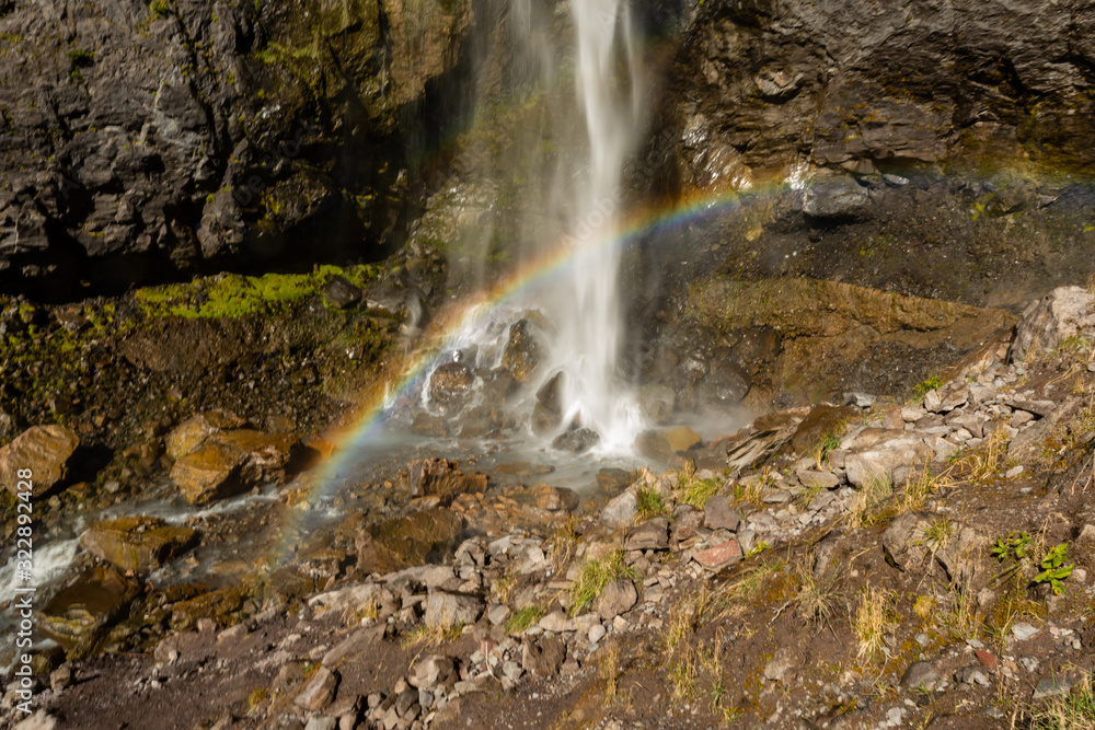 Fototapeta premium Rainbow Spans Across Base of Waterfall