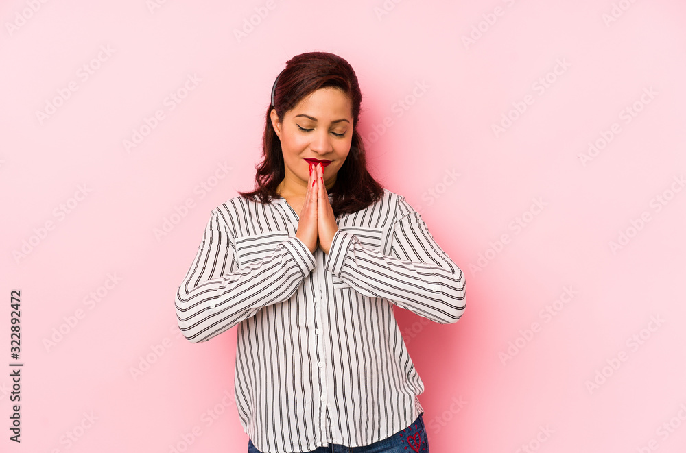 Middle age latin woman isolated on a pink background holding hands in pray near mouth, feels confident. Middle age latin woman isolated on a pink background holding hands in pray near mouth, feels confident.