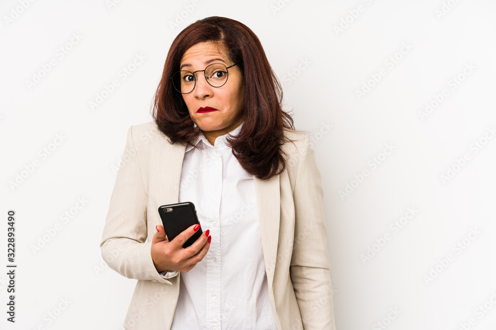 Middle age latin woman holding a mobile phone isolated shrugs shoulders and open eyes confused. Middle age latin woman holding a mobile phone isolated shrugs shoulders and open eyes confused.