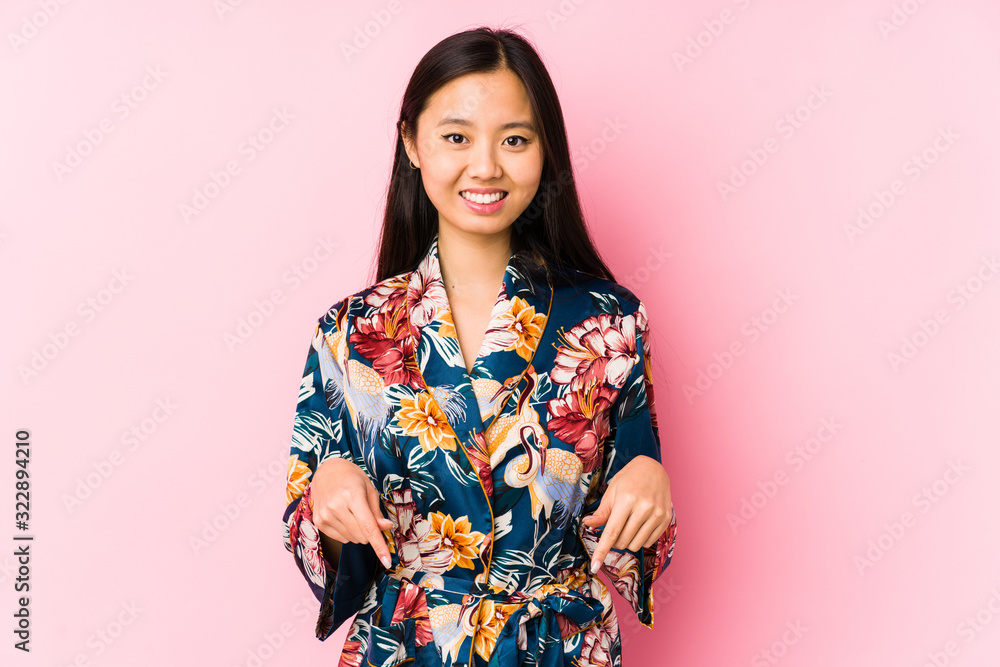 Young chinese woman wearing a kimono pajama isolated points down with fingers, positive feeling. Young chinese woman wearing a kimono pajama isolated points down with fingers, positive feeling.