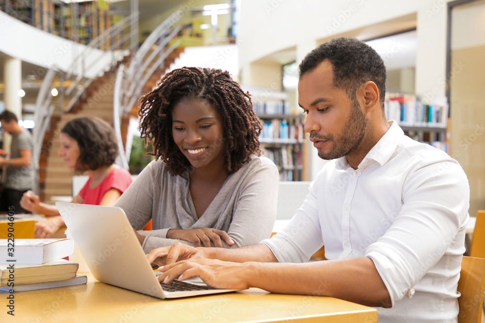 Cheerful young people working with laptop at library. Two joyful students working together. Education concept Cheerful young people working with laptop at library. Two joyful students working together. Education concept